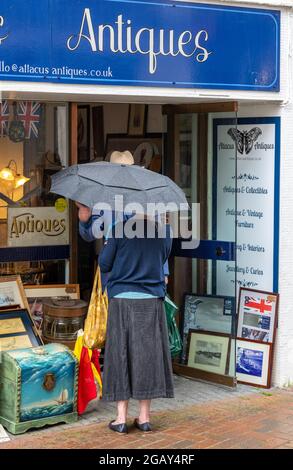 Older couple chatting outside of an antiques shop in the high street, middle aged couple chatting under umbrella, couple under umbrella, sheltering Stock Photo