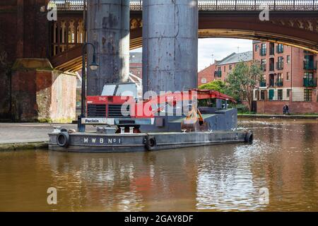 Black floating barge with a Poclain TP 45 crane moored by the Bridgewater Canal Tow Path in Castlefield, Manchester, north-west England, UK