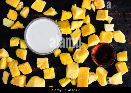 Mango Coconut Milkshake Ingredients on a Dark Wood Background: Frozen chunks of mango, coconut milk, and maple syrup Stock Photo