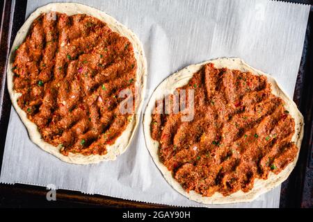 Two Uncooked Turkish Lahmacun on a Parchment Paper Lined Sheet Pan: Overhead view of raw Turkish flatbreads topped with spiced ground meat Stock Photo