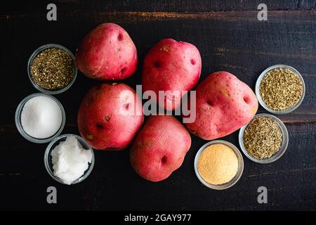 Tuscan Oven Roasted Red Potatoes Ingredients on a Wooden Table: Red potatoes, olive oil, and spices on a dark wood background Stock Photo