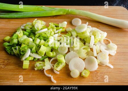 Closeup View of a Sliced Green Onion on a Bamboo Cutting Board: Slices of scallion on a wooden cutting board with a whole scallion in the background Stock Photo