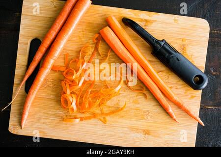 Peeling Carrots on a Bamboo Cutting Board: Overhead view of carrots and a vegetable peeler on a wooden cutting board Stock Photo