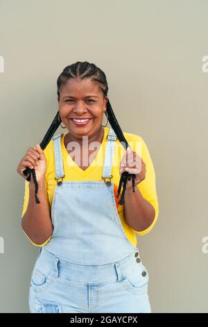 African woman with long hair and braids standing on a gray wall - happiness Stock Photo