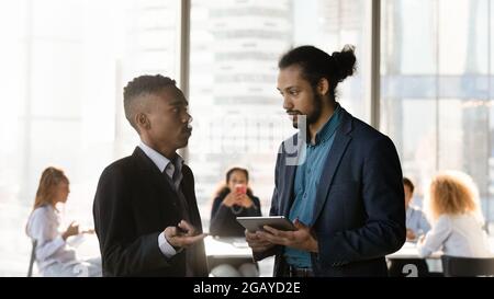 Concentrated two mixed race employees discussing online project results. Stock Photo