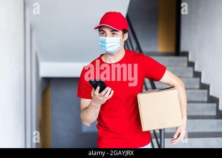 Delivery man courier online holding deliveries out boxes and using mobile phone contact the customer he protective face mask service under curfew quar Stock Photo