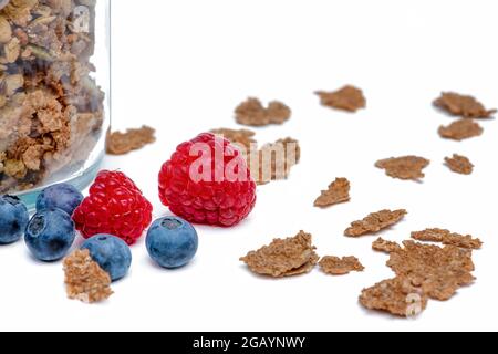 Isolate muesli. Dry muesli flakes with raspberries and blueberries lie on an isolated white background. Breakfast cereals in a glass jar on a white Stock Photo