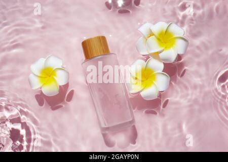 Glass bottle with plumeria flowers in rose water background. Splash of water. Stock Photo