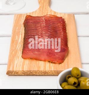 Cutting board with sliced dry salami on white table and olives Stock Photo