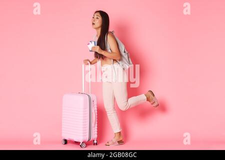 Travelling, holidays and vacation concept. Full-length of worried running asian girl tourist being late for her flight, carry suitcase and backpack Stock Photo