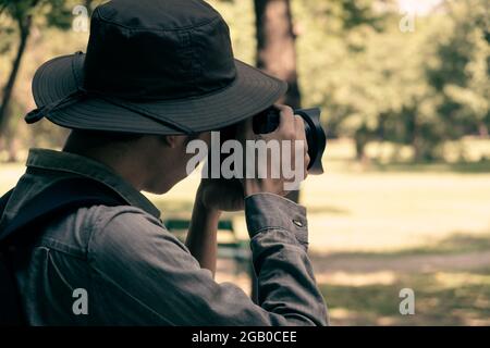 A young man hand holding a camera for take photo in a green natural place in his  holiday travel destination as shooting photograph trip in the concep Stock Photo