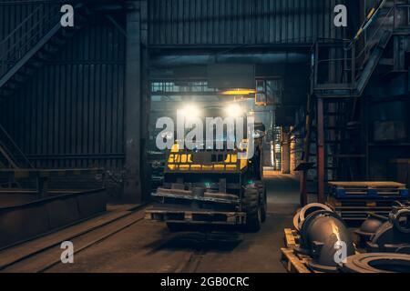 Small yellow loading tractor or mower at work in metallurgical factory workshop. Stock Photo