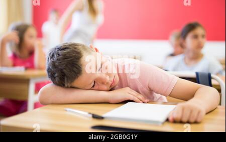 Tired preteen schoolboy sleeping at desk in classroom Stock Photo