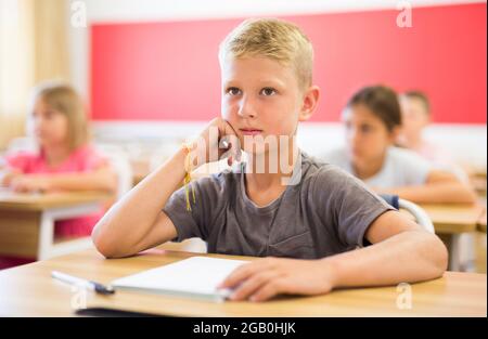 Focused preteen schoolboy writing in workbook at lesson in classroom Stock Photo