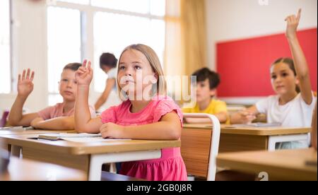 Diligent preteen schoolgirl raising hand to answer at lesson Stock Photo