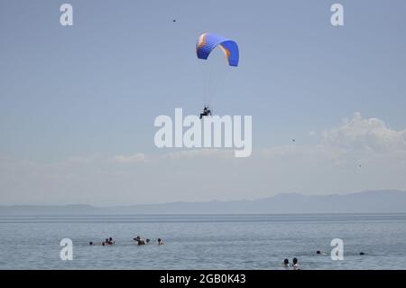 Para glider with a propeller on his back flying over blue water with swimmers. Stock Photo