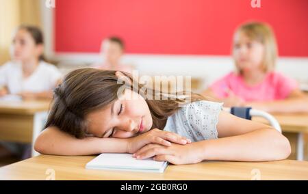 Tired preteen girl sleeping at desk at lesson in classroom Stock Photo