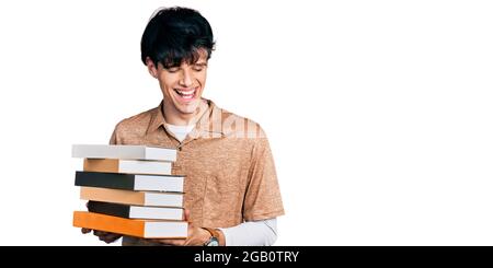 Handsome hipster young man holding a pile of books smiling and laughing hard out loud because funny crazy joke. Stock Photo