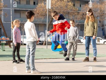 Energetic kids playing and skipping on elastic jumping rope in european yard Stock Photo