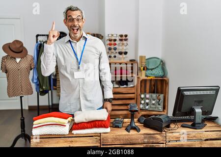Middle age hispanic man working as manager at retail boutique pointing finger up with successful idea. exited and happy. number one. Stock Photo