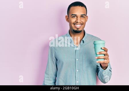 Young african american man drinking a take away cup of coffee looking positive and happy standing and smiling with a confident smile showing teeth Stock Photo