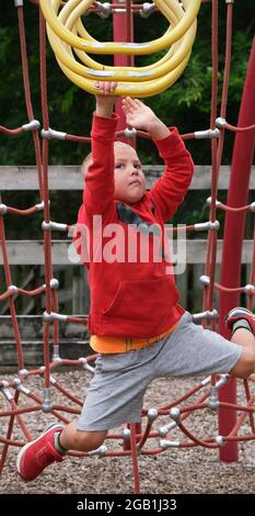 A 5 year old boy concentrates as he hangs from his arms and swings along a set of monkey bars. Stock Photo