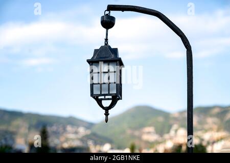 An old street lamp is hanging on a pole against the background of nature. Stock Photo
