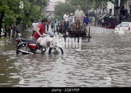 Pakistani commuters wade through a flooded street after heavy monsoon ...