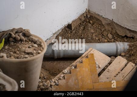 Leaking plastic sewage pipe in an old apartment, visible open hole with removed parquet, sand and buckets around, exposed drain pipe in the ground. Stock Photo