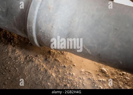 Leaking plastic sewage pipe in an old apartment, visible open hole with removed parquet, sand and buckets around, exposed drain pipe in the ground. Stock Photo