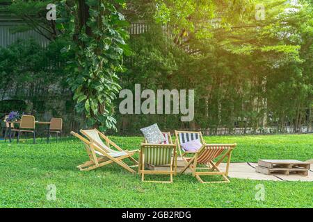 Many deck chairs and pillows with wooden table in the courtyard is surrounded by shady green grass. Comfortable pillows on outdoor patio chair and tab Stock Photo