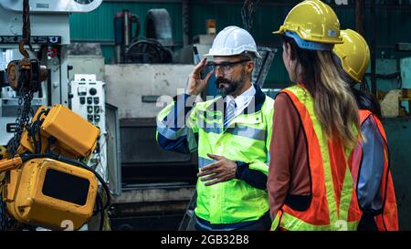 Mechanical engineer manager working in industry and factory control worker and introduce teamwork wearing safety reflective vest and  helmet to protec Stock Photo