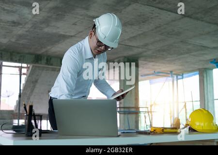 Engineer work and check on laptop in construction site, foreman wearing helmet and use computer to control and design building construction Stock Photo