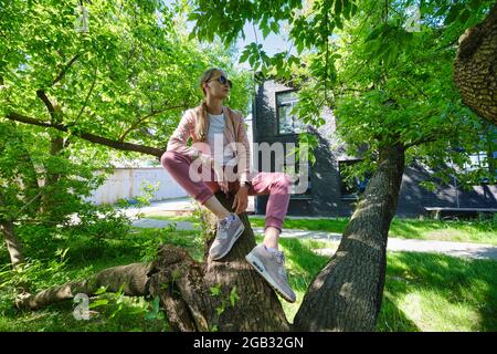 Young woman sits on crooked tree trunk in sunny day Stock Photo