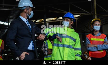 Industry factory manager greeting with assistant and worker by touch with elbow Stock Photo