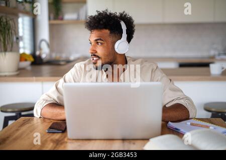 Young man student with laptop and headphones indoors at home, studying. Stock Photo