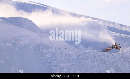 A snow blower car clears snow in on the mountain from the road on a winter. Snow plow truck cleaning icy white road. Stock Photo