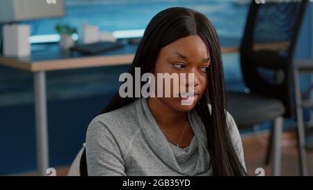 University student writing math lesson on notebook while searching online webinar sitting on bean bag in living room. Teenager with dark skin studying business, working from home, computer user Stock Photo