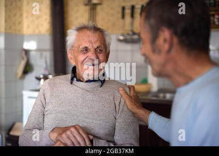 Portrait of man with elderly father sitting at the table indoors at home, talking. Stock Photo