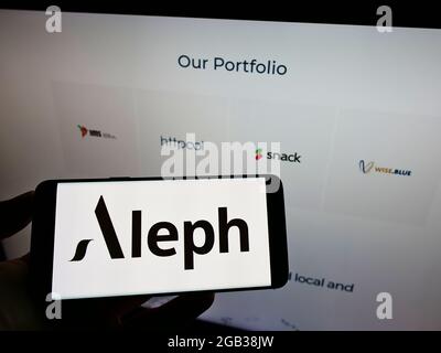Person holding cellphone with logo of US digital media company Aleph Holding on screen in front of business webpage. Focus on phone display. Stock Photo