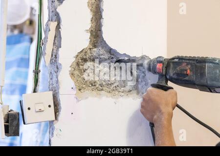 Worker drilling on wall to create cavity for electric power socket in home renovation. Motion blur intended. Stock Photo