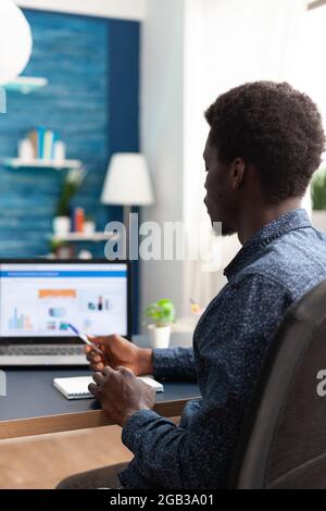 Black man working from home using financial economy data app on laptop. African american guy computer user using business workplace internet online website communication job lifestyle Stock Photo