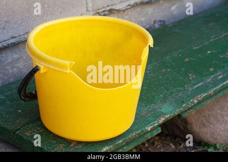 Empty dirty broken yellow plastic bucket on green bench Stock Photo