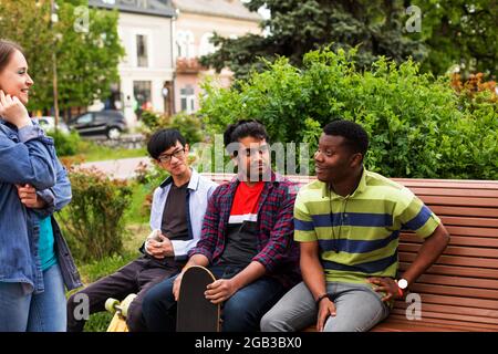 Excited diverse friends sitting on wooden bench Stock Photo