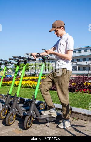 A young man rents an electric scooter by scanning the QR code with a smartphone. Kick scooters in sharing parking. Stock Photo