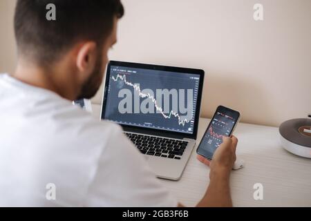 Young adult man trading on line with tablet pc connected to stock market. People, finance, investments. Over the shoulders Stock Photo