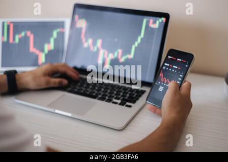 Close up of male earning money by online traind in. Man using laptop, tablet and phone for monitor grows cryptocurrency stocks. Home finances Stock Photo