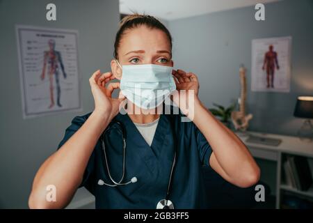Caucasian female nurse wearing surgical mask standing in doctors clinic Stock Photo