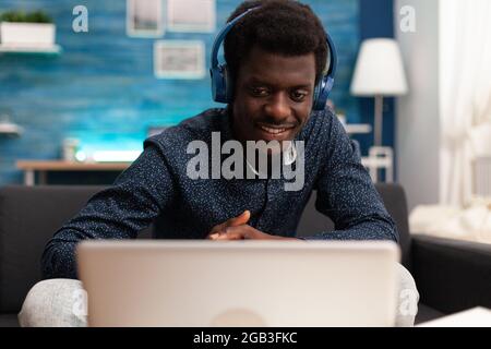 Black man using headphones and laptop technology for internet website services. African american person working from home with modern gadgets and communication devices on business Stock Photo