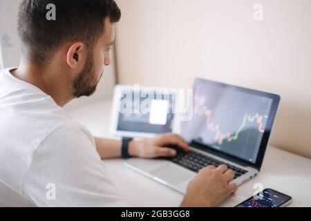 Man looking at finance chart on laptop and tablet, day trader, investing from home. Young man monitors his investments. Ambitious businessman Stock Photo